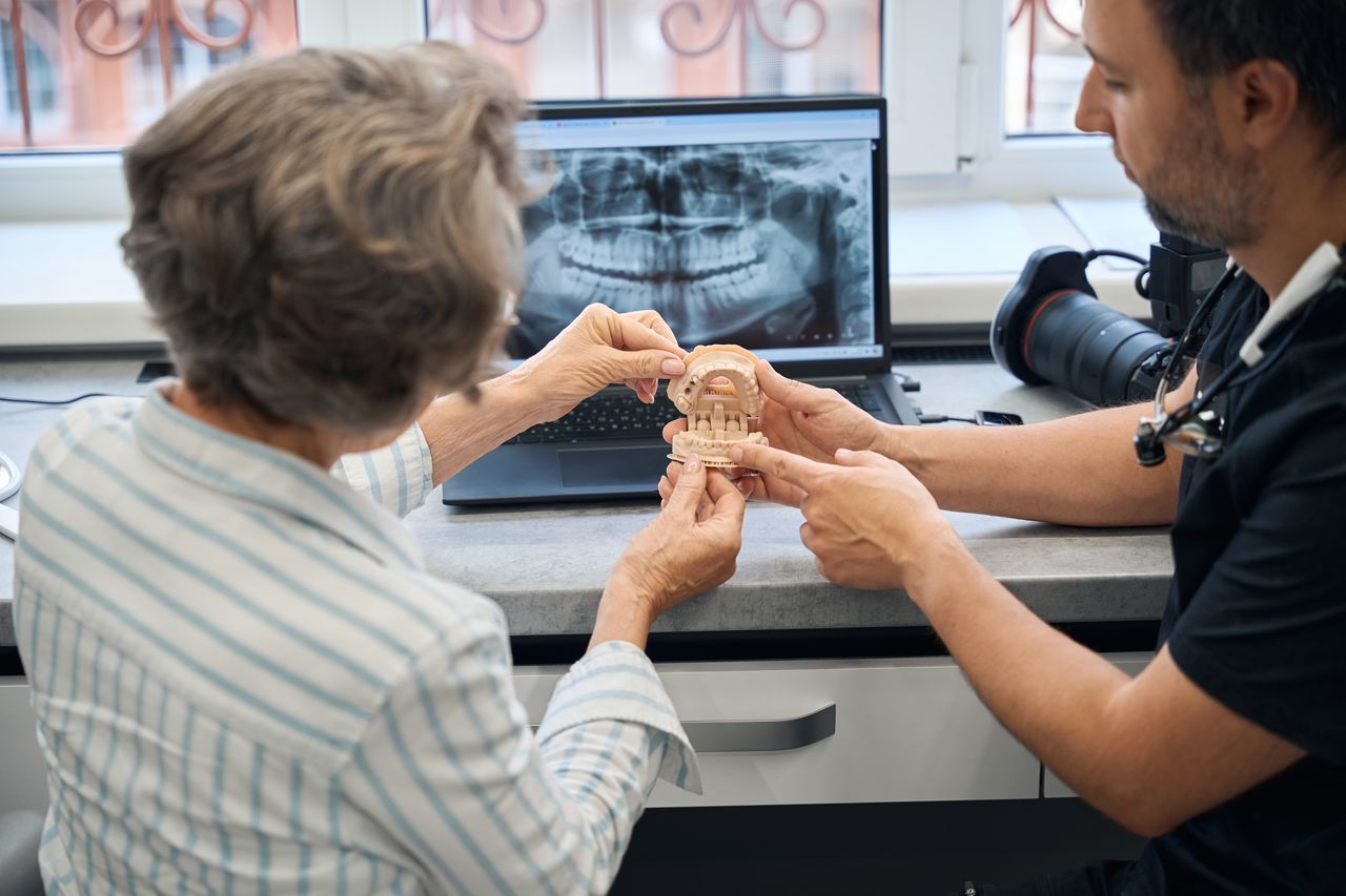Un dentiste explique un implant dentaire à sa patiente à l'aide d'un modèle